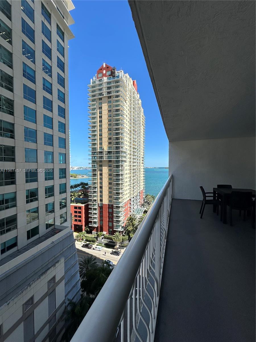 A balcony with outdoor furniture overlooks a city street and a tall waterfront high-rise building — 1200 Brickell Bay Dr # 1712, Miami FL 33131, MIAMI, FL