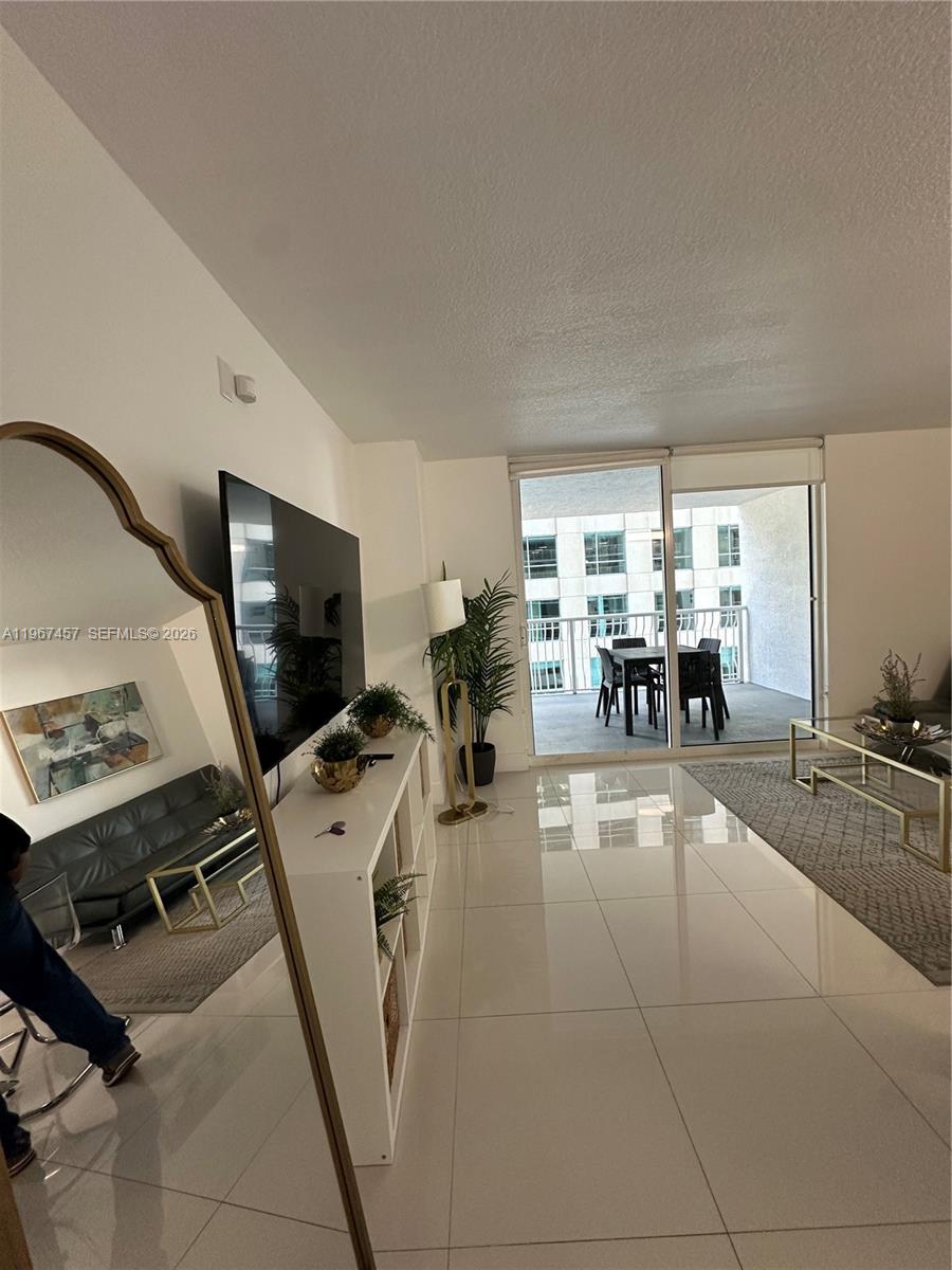 A living room features white tile floors, a large television, and a balcony with seating — 1200 Brickell Bay Dr # 1712, Miami FL 33131, MIAMI, FL
