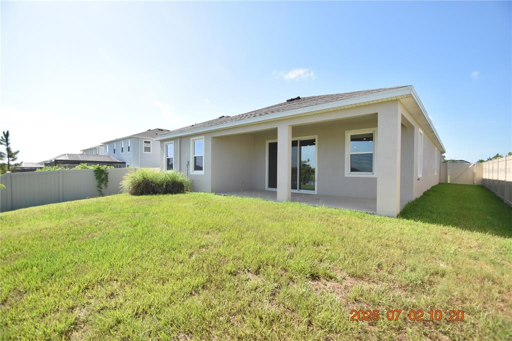 The exterior of a house features a covered patio, a grassy yard, and vinyl fencing — 32003 CONCHSHELL SAIL STREET, WESLEY CHAPEL, FL