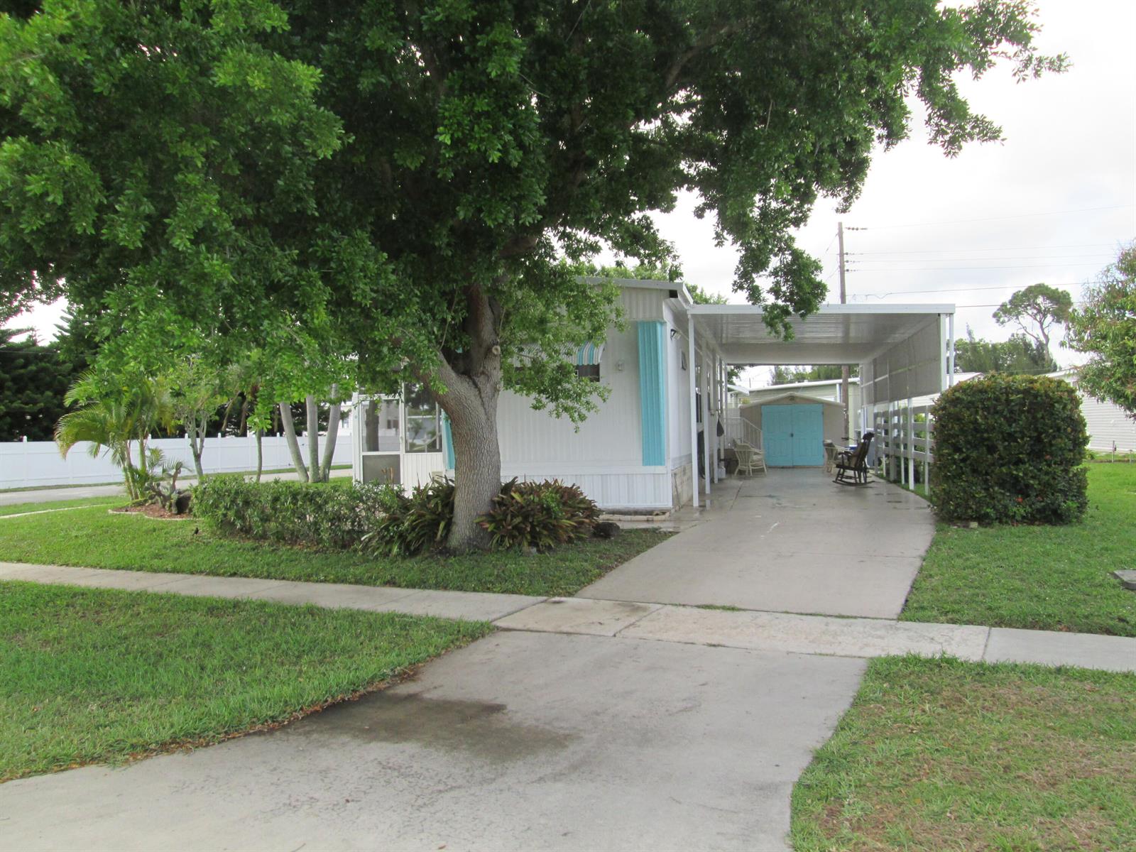 A white mobile home features a large shade tree, a carport, and a blue shed — 4261 Meadow View Drive, Boynton Beach FL 33436, BOYNTON BEACH, FL