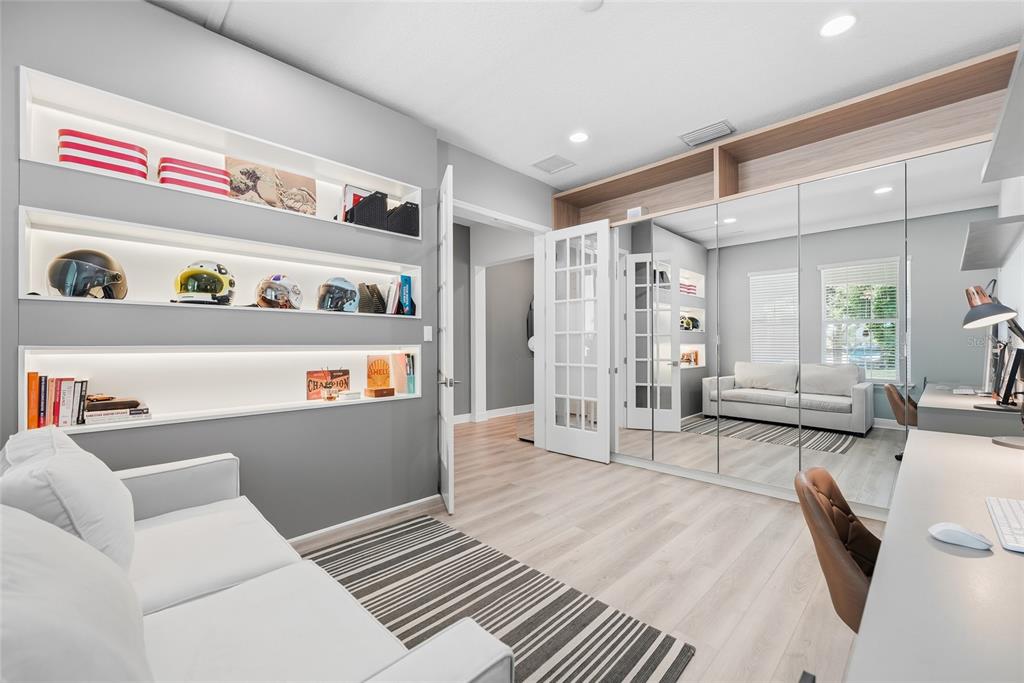 A home office features built-in illuminated shelving, mirrored closet doors, a sofa, and wood flooring — 15790 SWEET LIMETTA DRIVE, WINTER GARDEN, FL