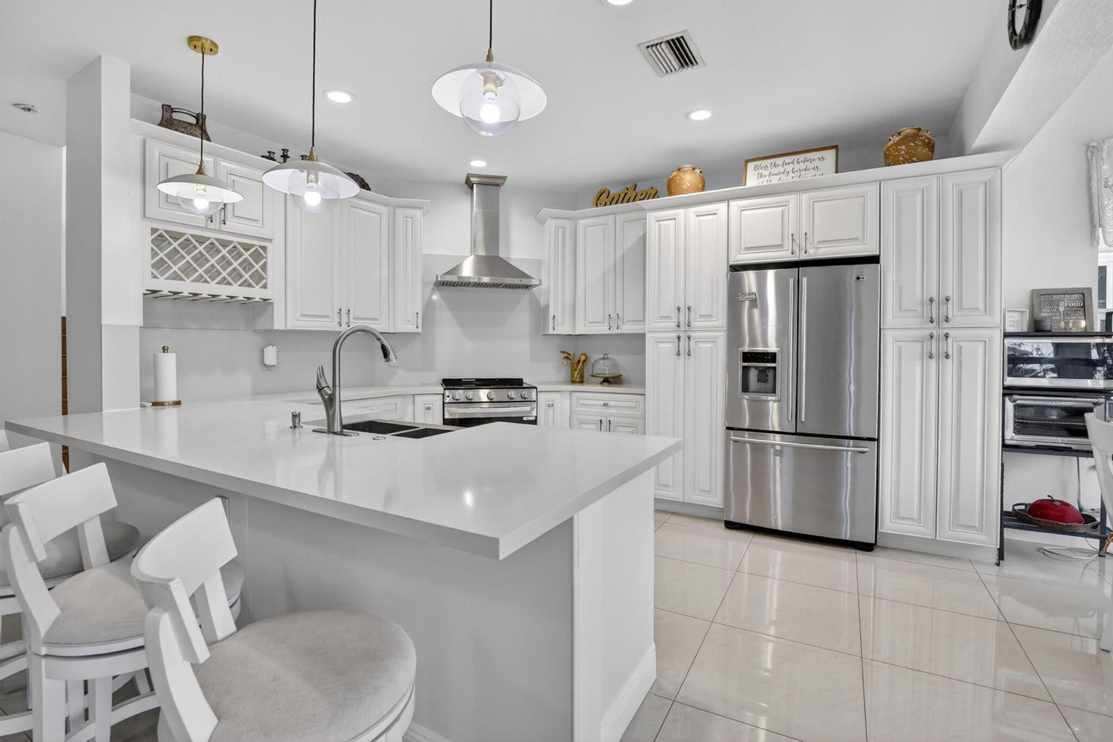A bright kitchen features white cabinetry, stainless steel appliances, a large island, and tile flooring — 711 Heritage Way, Weston FL 33326, WESTON, FL