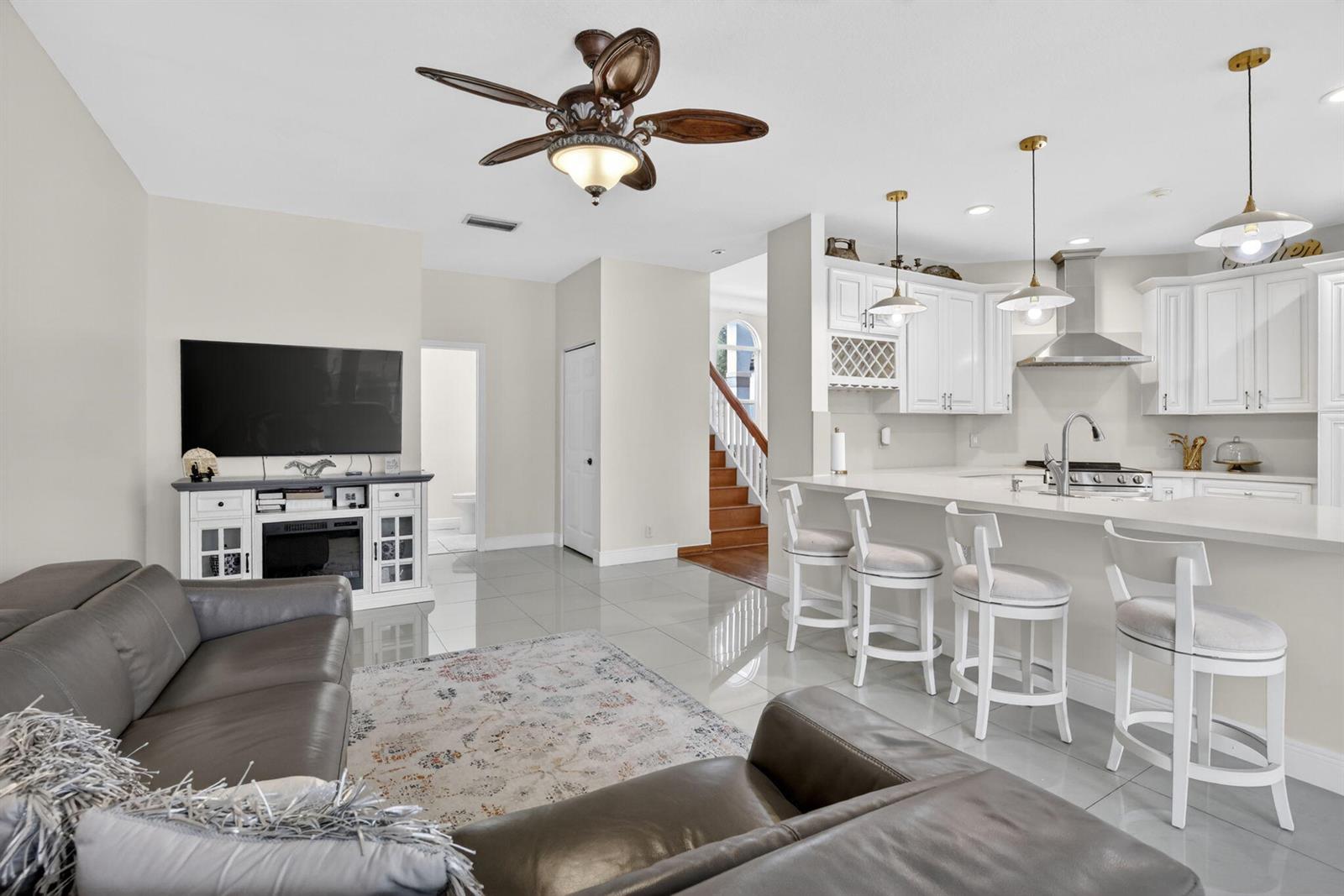 A living room with a grey sofa and TV console opens to a white kitchen — 711 Heritage Way, Weston FL 33326, WESTON, FL