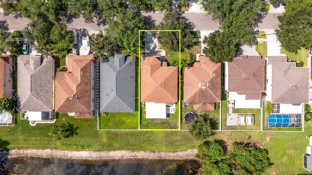 An aerial view shows a residential house with a brown roof and backyard facing a pond — 18923 FISHERMANS BEND DRIVE, LUTZ, FL