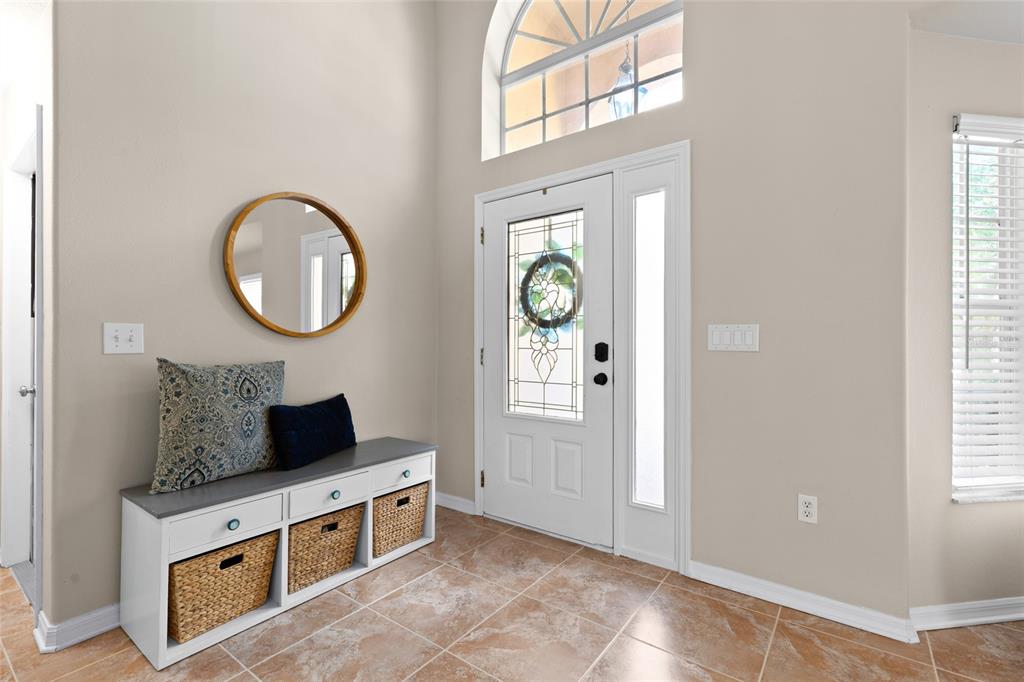 A bright entryway features tile flooring, a white storage bench, a round mirror, and a door — 18923 FISHERMANS BEND DRIVE, LUTZ, FL