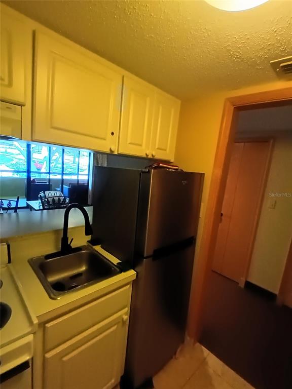 A small kitchen features white cabinets, a stainless steel refrigerator, and a single-basin sink — 36750 US HIGHWAY 19 N UNIT 13-216, PALM HARBOR, FL