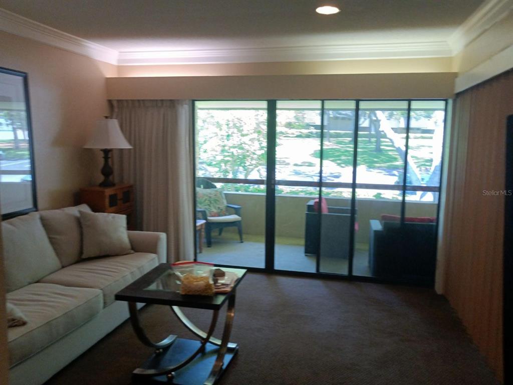 A living room with a beige sofa, glass coffee table, and sliding doors to a balcony — 36750 US HIGHWAY 19 N UNIT 13-216, PALM HARBOR, FL