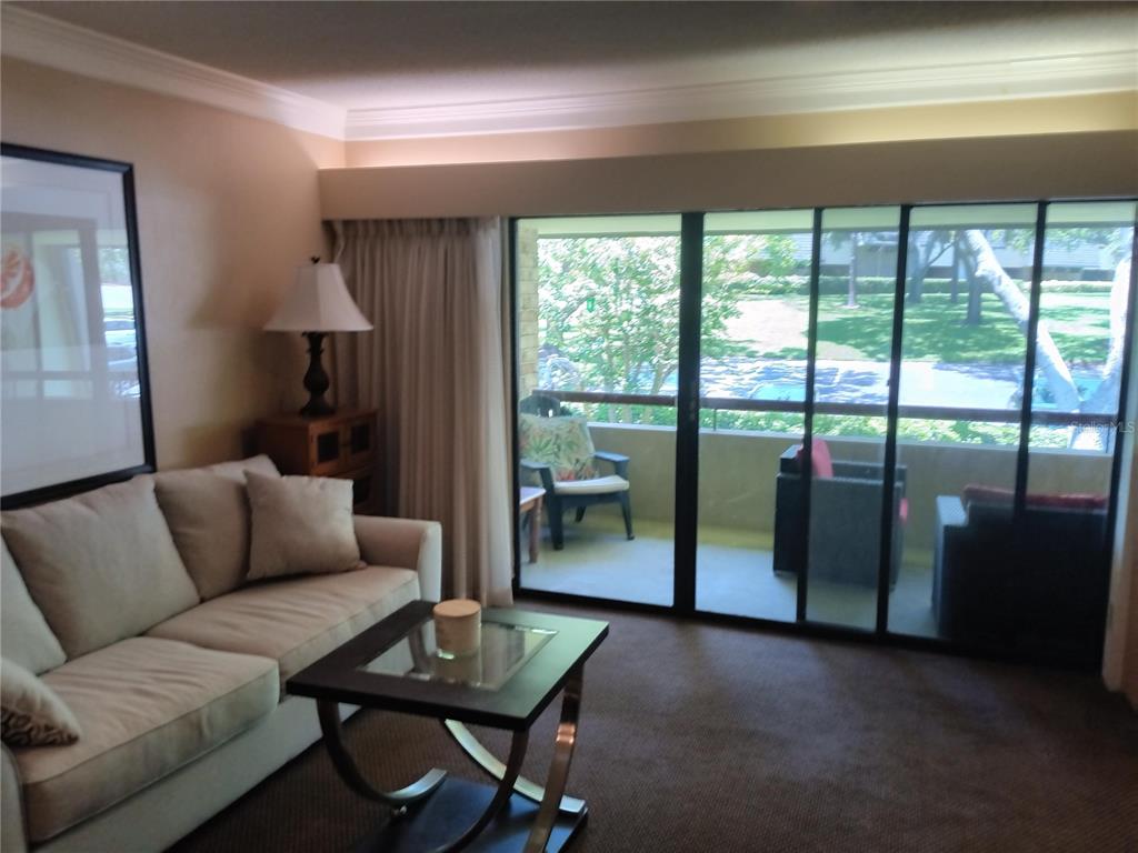 A living room with a sofa, glass-topped coffee table, and sliding doors leading to a balcony — 36750 US HIGHWAY 19 N UNIT 13-216, PALM HARBOR, FL