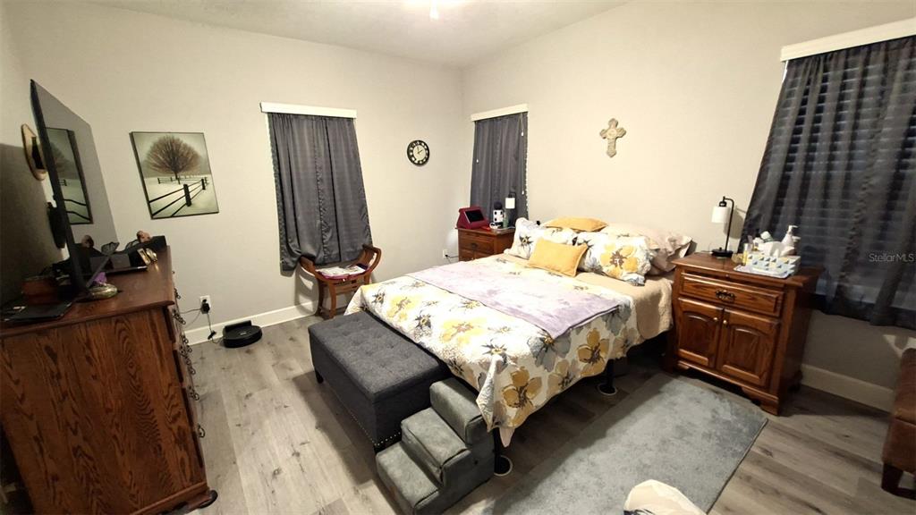 A bedroom features a bed with floral bedding, a wooden dresser, and gray wood-look flooring — 20074 NW 249TH STREET, HIGH SPRINGS, FL