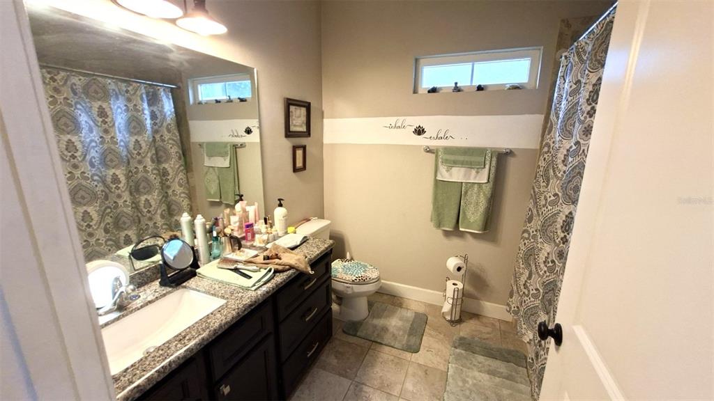 A bathroom features a dark wood vanity, granite countertop, toilet, and a patterned shower curtain — 20074 NW 249TH STREET, HIGH SPRINGS, FL