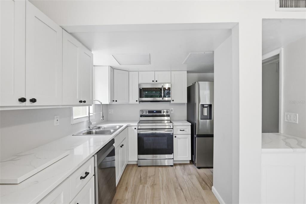 A kitchen features white cabinets, stainless steel appliances, and light wood-look flooring — 100 FAIRWAY DRIVE UNIT 100, LONGWOOD, FL