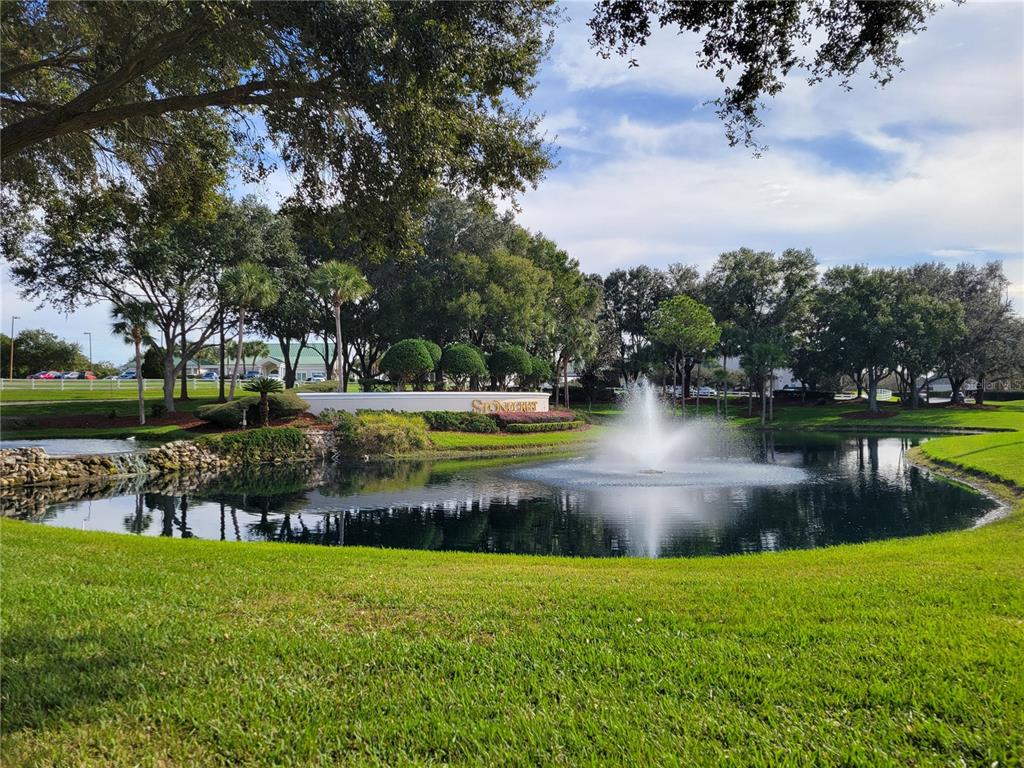 A fountain sits in a pond in front of a stone entrance sign with landscaping — 11227 SE 172ND PLACE, SUMMERFIELD, FL
