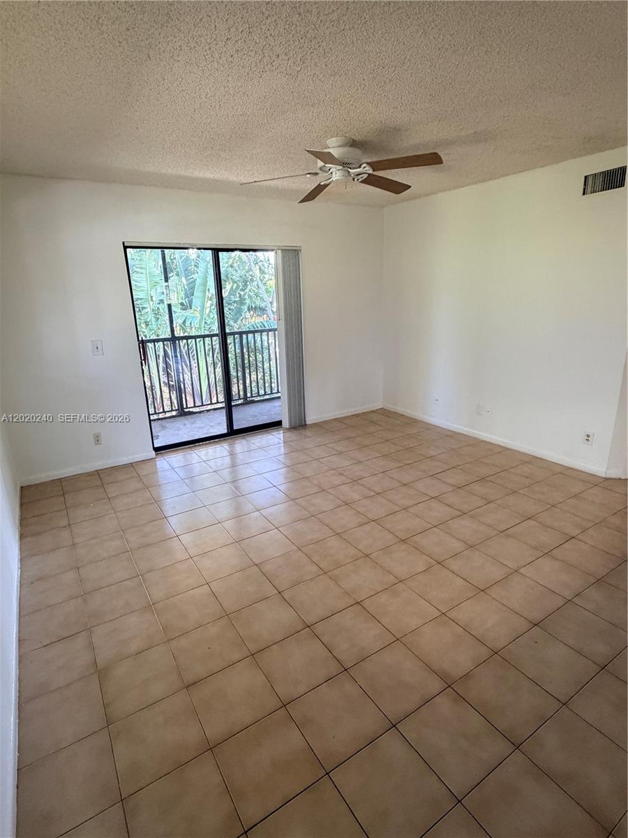 An empty room features beige tile flooring, white walls, a ceiling fan, and a sliding glass door — 588 Trace Cir # 202, Deerfield Beach FL 33441, DEERFIELD BEACH, FL