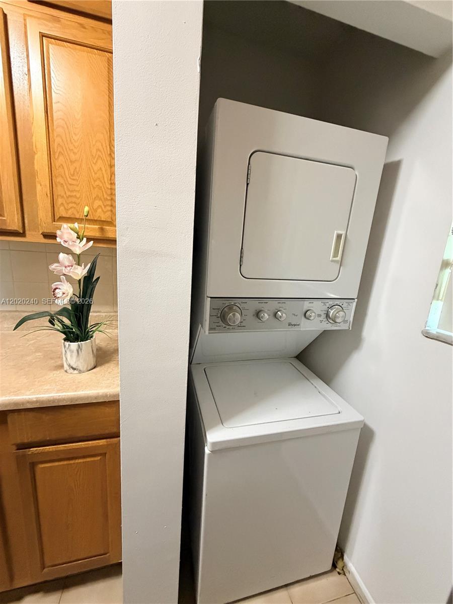 A stacked white Whirlpool washer and dryer unit sits in a small laundry alcove — 588 Trace Cir # 202, Deerfield Beach FL 33441, DEERFIELD BEACH, FL