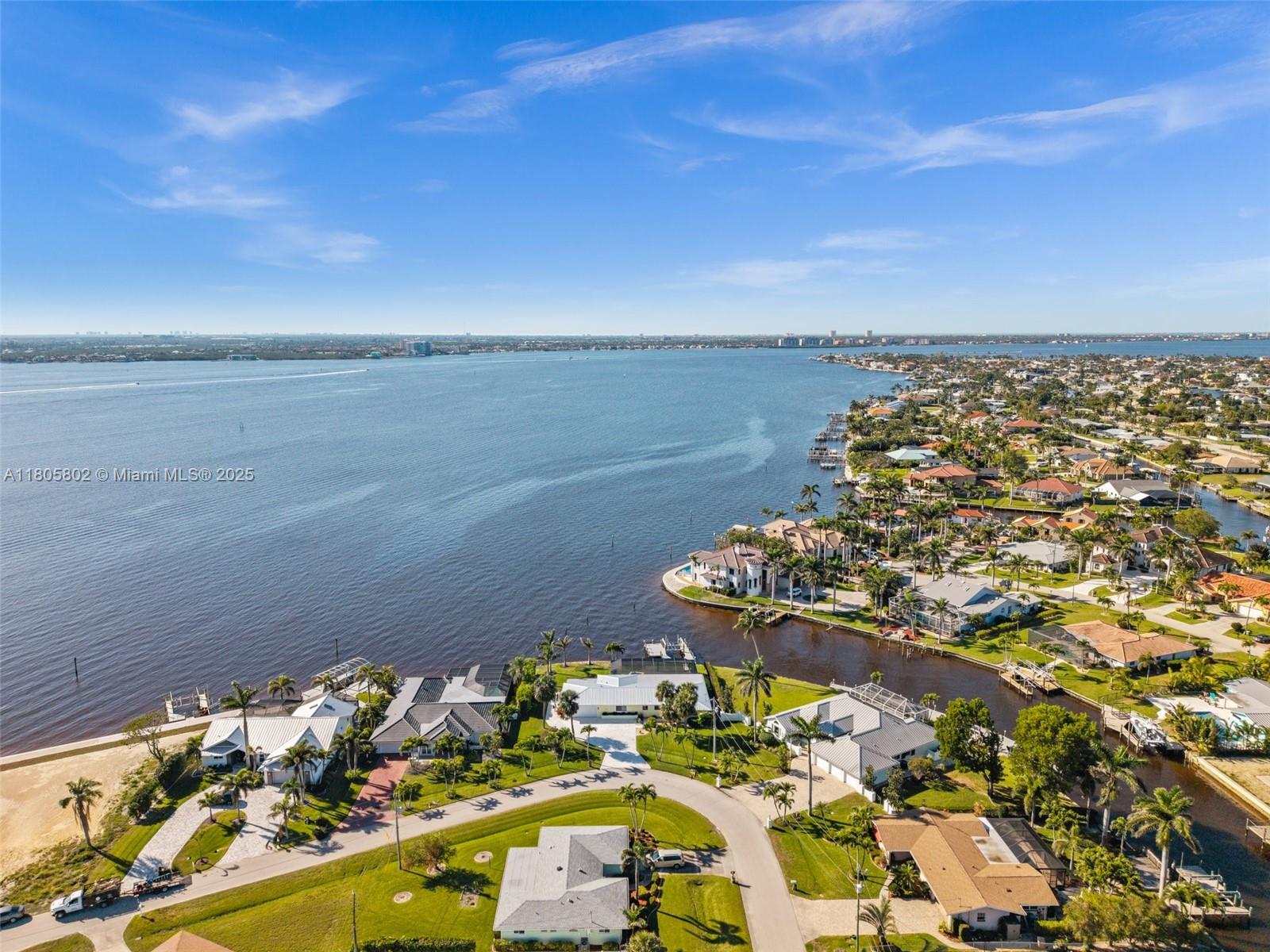 An aerial view shows waterfront homes along a canal leading into a large bay — 1600 Edith Esplanade, Cape Coral FL 33904, CAPE CORAL, FL