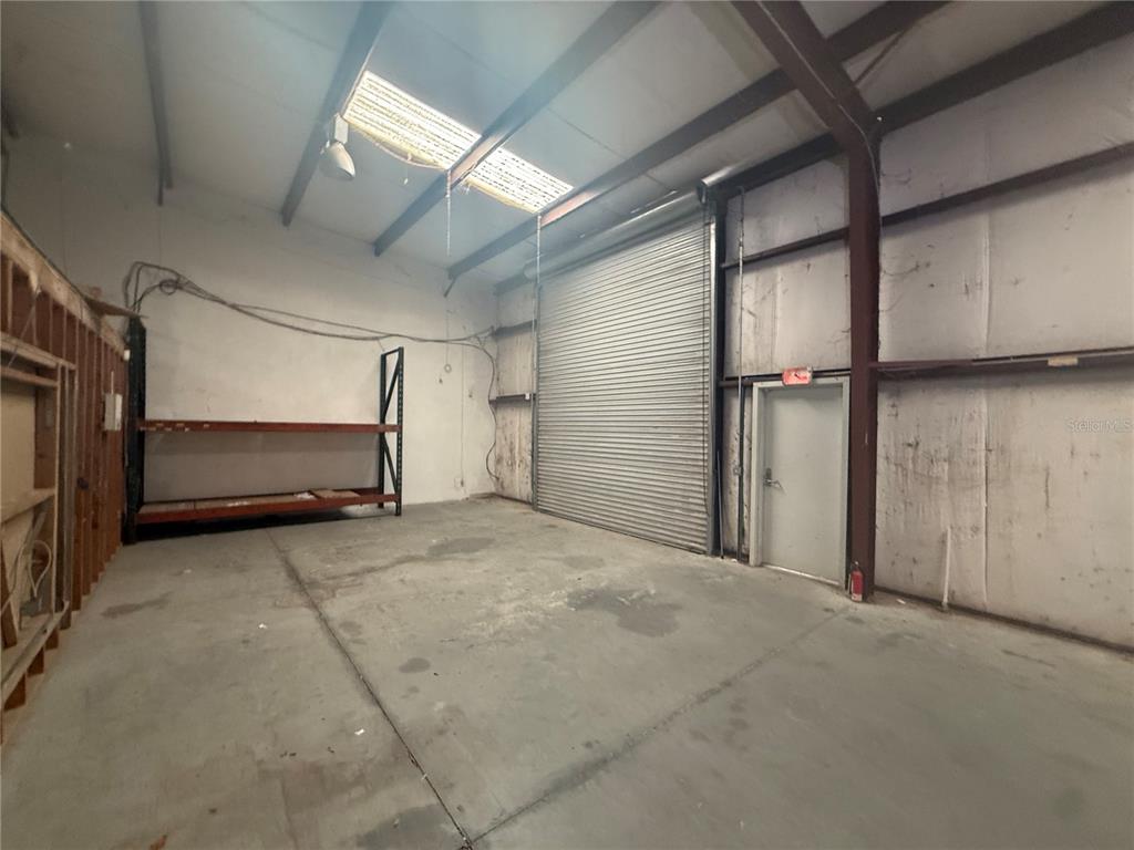 An industrial warehouse space features a concrete floor, metal roll-up door, and metal shelving — 4344 SE 95TH STREET UNIT 2, OCALA, FL