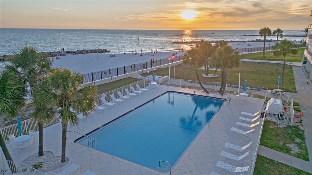 An elevated view of a rectangular swimming pool with lounge chairs overlooking a sandy beach — 7000 BEACH PLAZA UNIT 202, ST PETE BEACH, FL