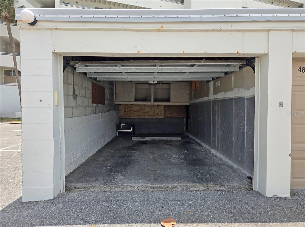 An open, unfinished concrete garage with exposed block walls and a metal overhead door — 7000 BEACH PLAZA UNIT 202, ST PETE BEACH, FL