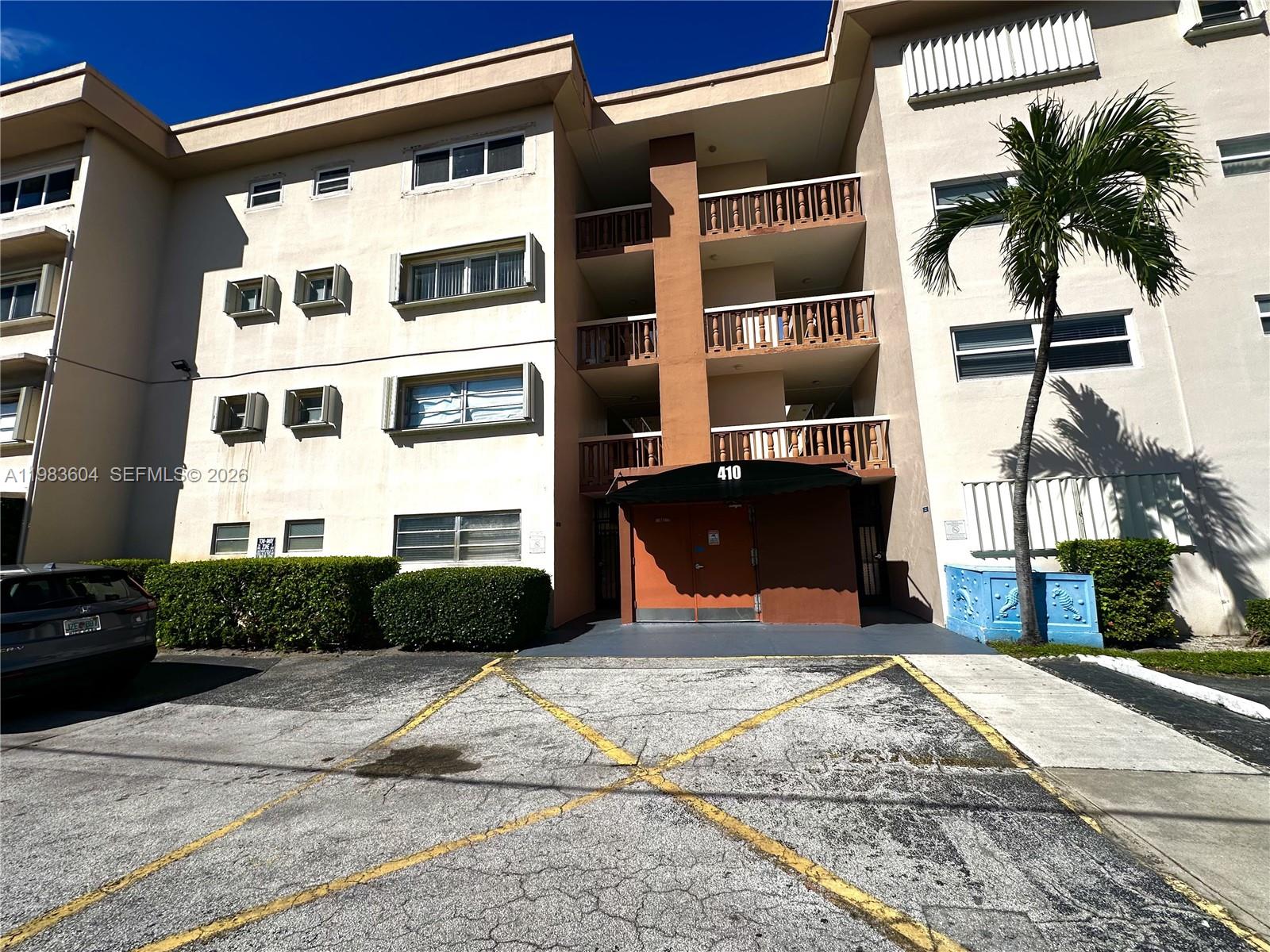 The exterior of a multi-story apartment building features a central entrance with a brown awning — 410 SE 2nd St # 102, Hallandale Beach FL 33009, HALLANDALE BEACH, FL