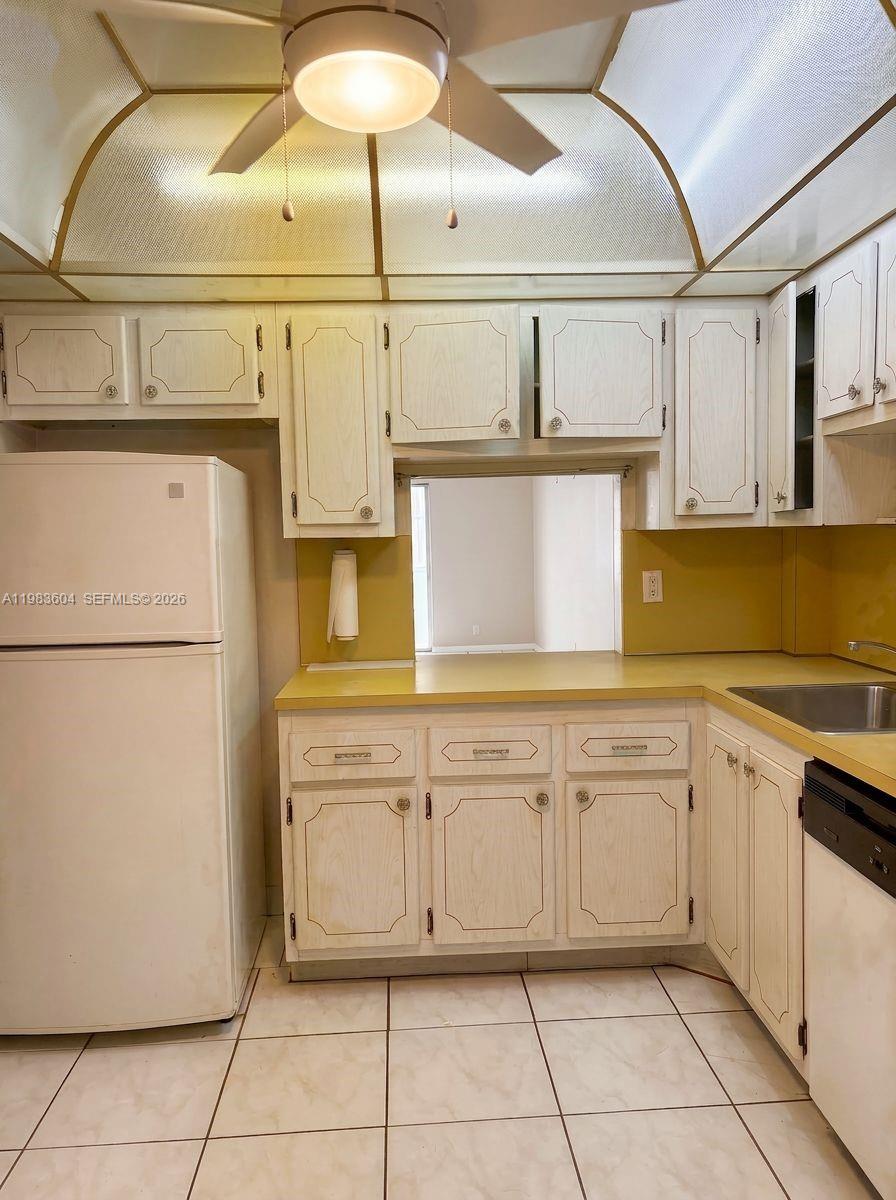 A kitchen features white cabinets, yellow countertops, a white refrigerator, and a ceiling fan — 410 SE 2nd St # 102, Hallandale Beach FL 33009, HALLANDALE BEACH, FL