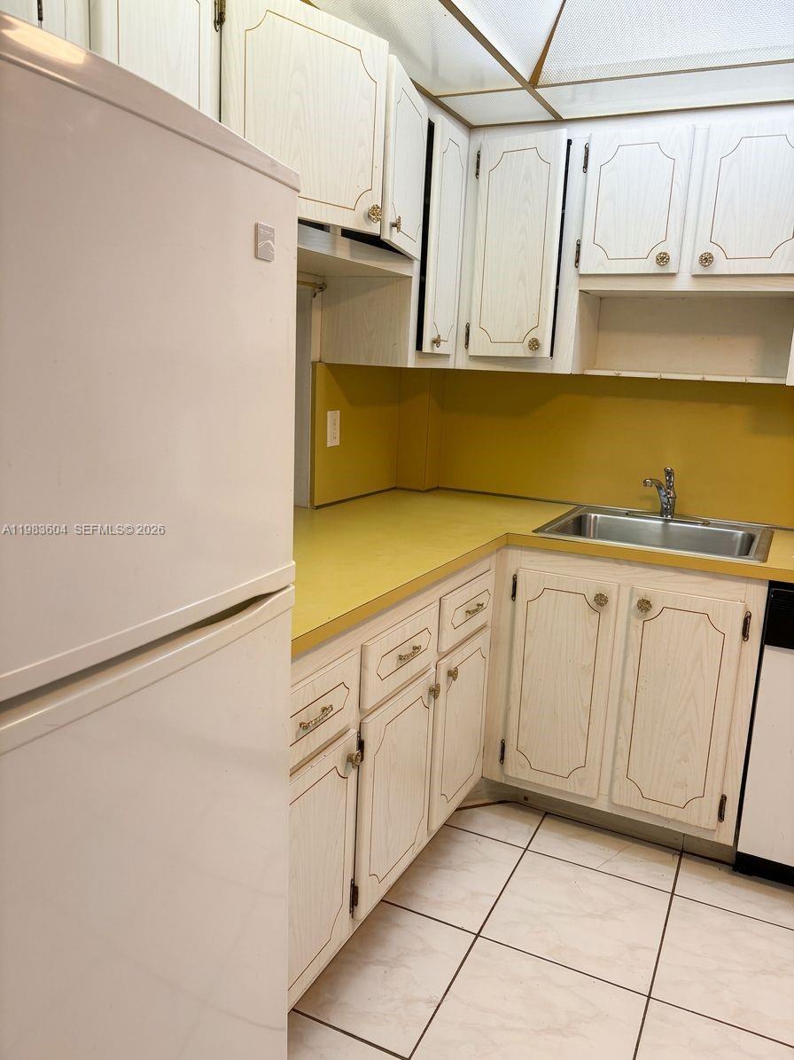 A kitchen features white cabinets, a yellow countertop, a white refrigerator, and tiled flooring — 410 SE 2nd St # 102, Hallandale Beach FL 33009, HALLANDALE BEACH, FL