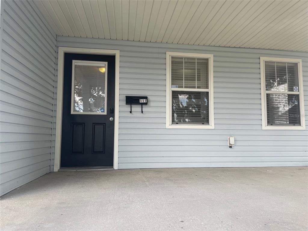 A light blue house exterior features a dark front door and two windows under a porch — 111 S RANDOLPH AVENUE, KISSIMMEE, FL