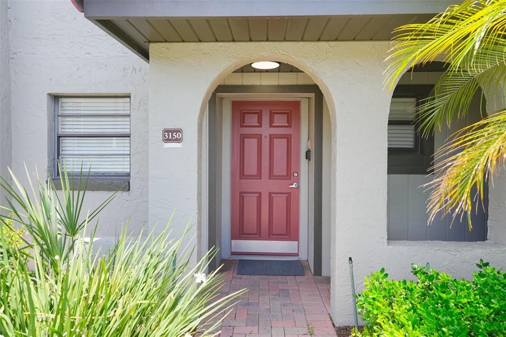 A red front door with a silver kickplate is centered under an arched entryway — 3150 WET N WILD COURT, KISSIMMEE, FL