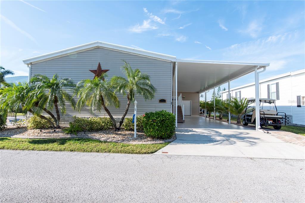 A light gray manufactured home features a carport, palm trees, and a decorative wall star — 1 DEN HELDER AVENUE, PUNTA GORDA, FL