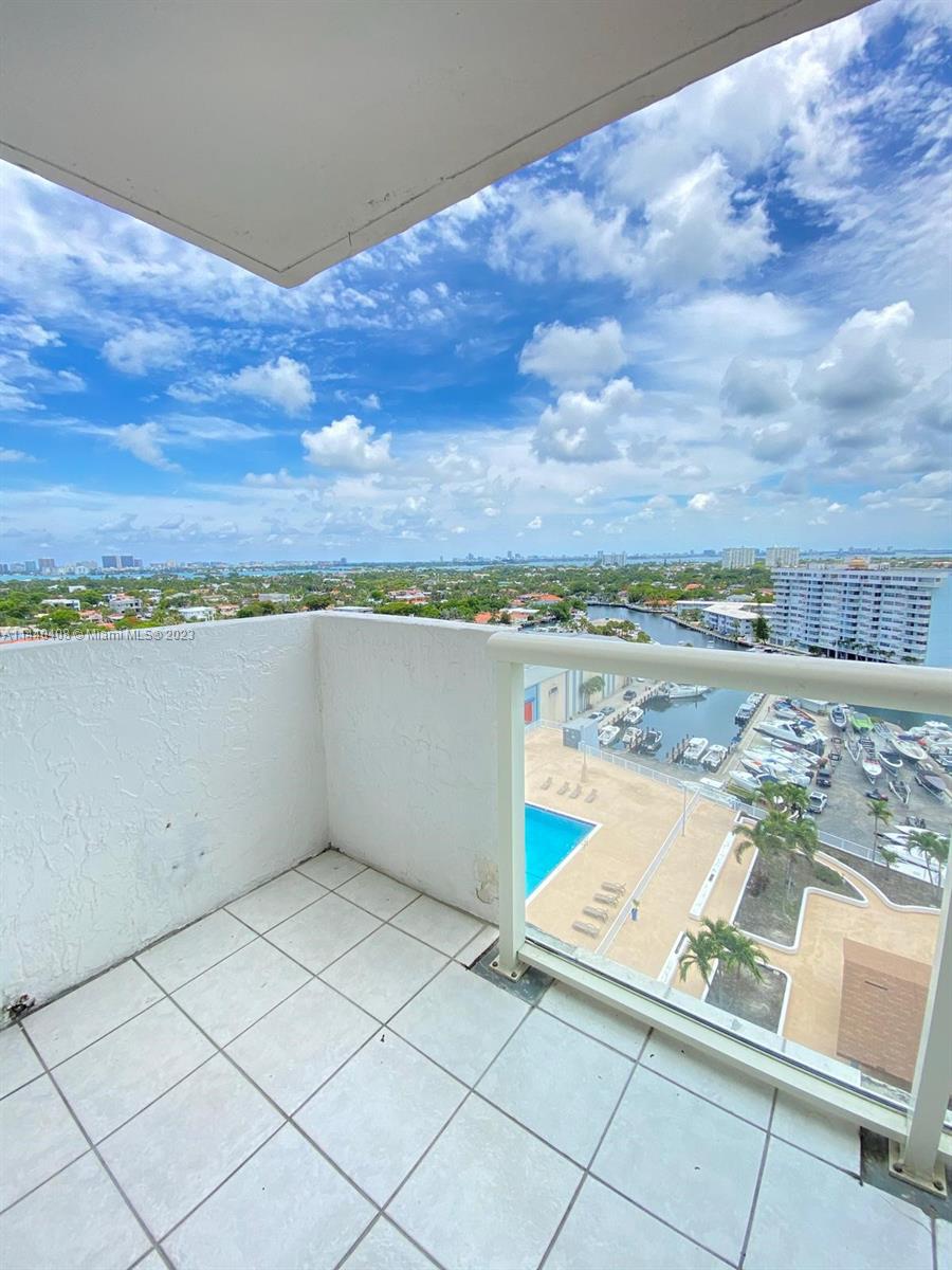 A high-angle view from a tiled balcony overlooking a swimming pool and a boat marina — 13499 Biscayne Blvd # 1408, North Miami FL 33181, NORTH MIAMI, FL