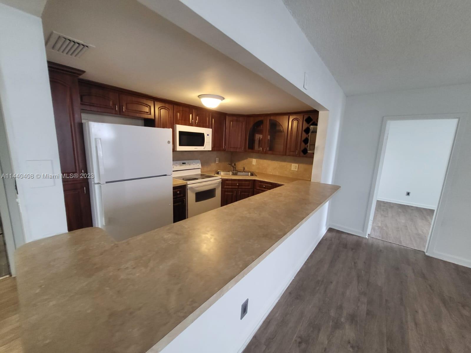 A kitchen with dark wood cabinets, white appliances, and a breakfast bar counter — 13499 Biscayne Blvd # 1408, North Miami FL 33181, NORTH MIAMI, FL