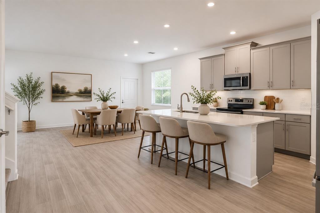 A modern kitchen with gray cabinets, a white island, and an adjacent dining area — 12018 LANGUAGE WAY, ORLANDO, FL