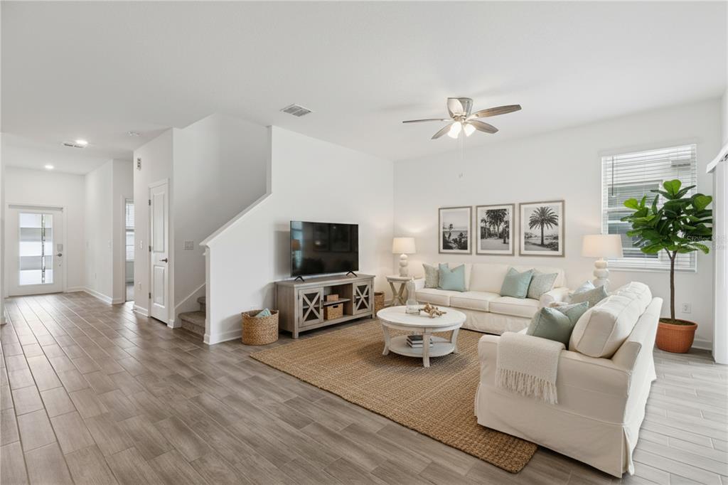 A bright living room features white walls, wood-look tile flooring, and neutral-toned furniture — 12018 LANGUAGE WAY, ORLANDO, FL
