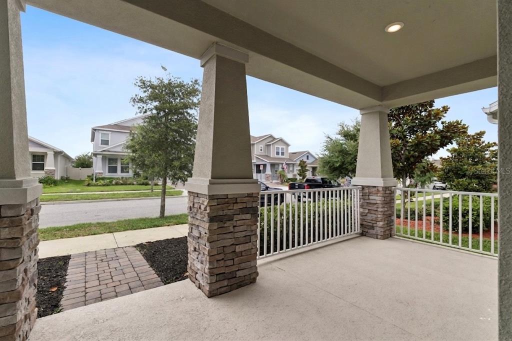 A covered front porch features stone-based columns, a white railing, and a concrete floor — 12018 LANGUAGE WAY, ORLANDO, FL