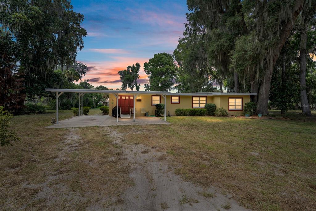 A single-story yellow house with a carport and a red front door under large trees — 2345 CR 453, LAKE PANASOFFKEE, FL