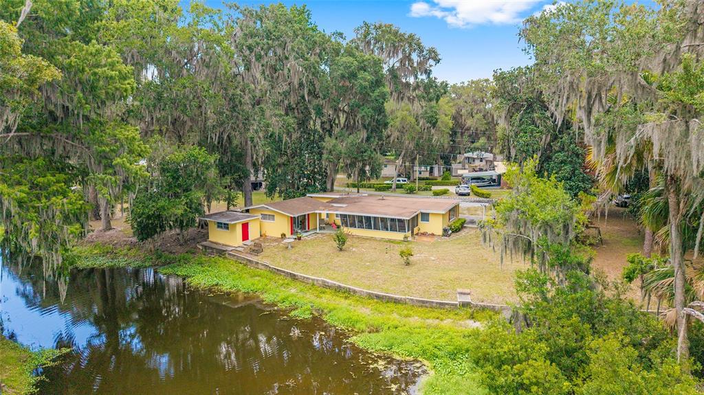 An aerial view of a yellow single-story house situated beside a canal with mature trees — 2345 CR 453, LAKE PANASOFFKEE, FL