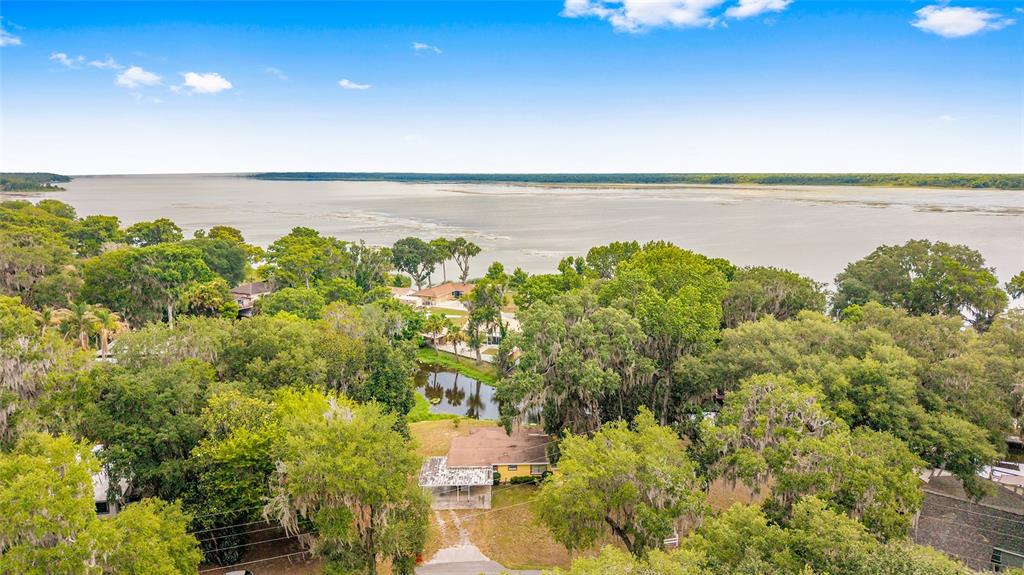 An aerial view shows a house surrounded by trees near a large body of water — 2345 CR 453, LAKE PANASOFFKEE, FL