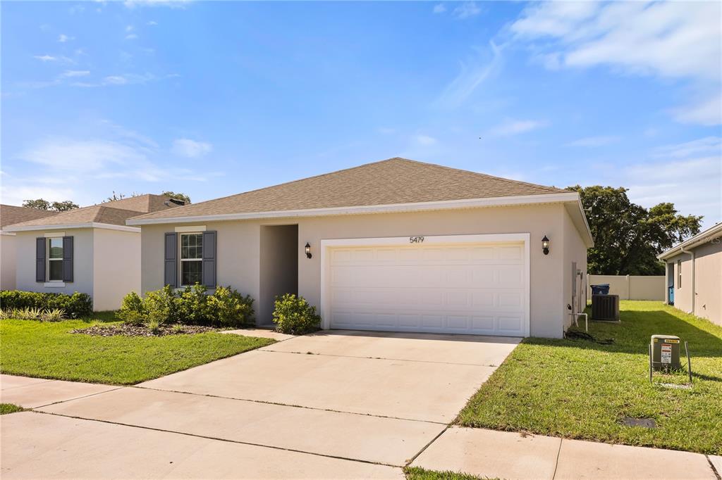 A single-story house with a beige stucco exterior, a two-car garage, and a concrete driveway — 5479 MADDIE DRIVE, HAINES CITY, FL