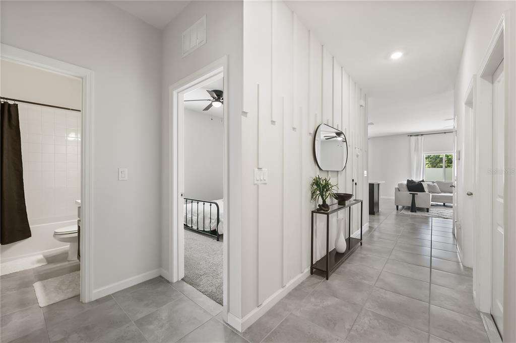 A hallway with gray tile flooring leads to a living area past a bedroom doorway — 5479 MADDIE DRIVE, HAINES CITY, FL