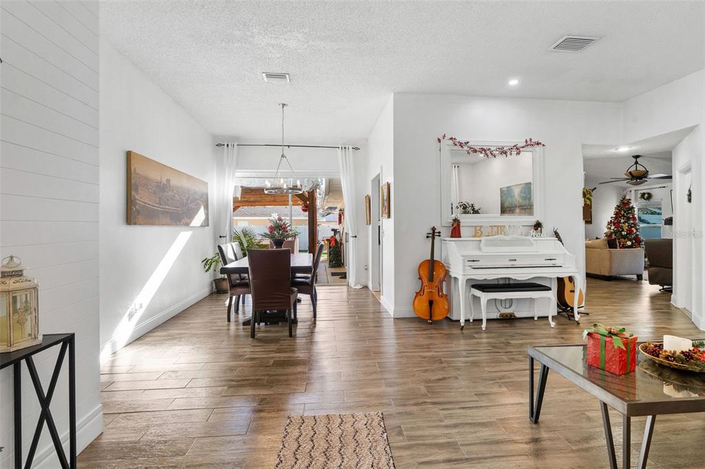 A bright living and dining area features wood-look tile floors, a white piano, and patio access — 15101 REDVALE DRIVE, TAMPA, FL
