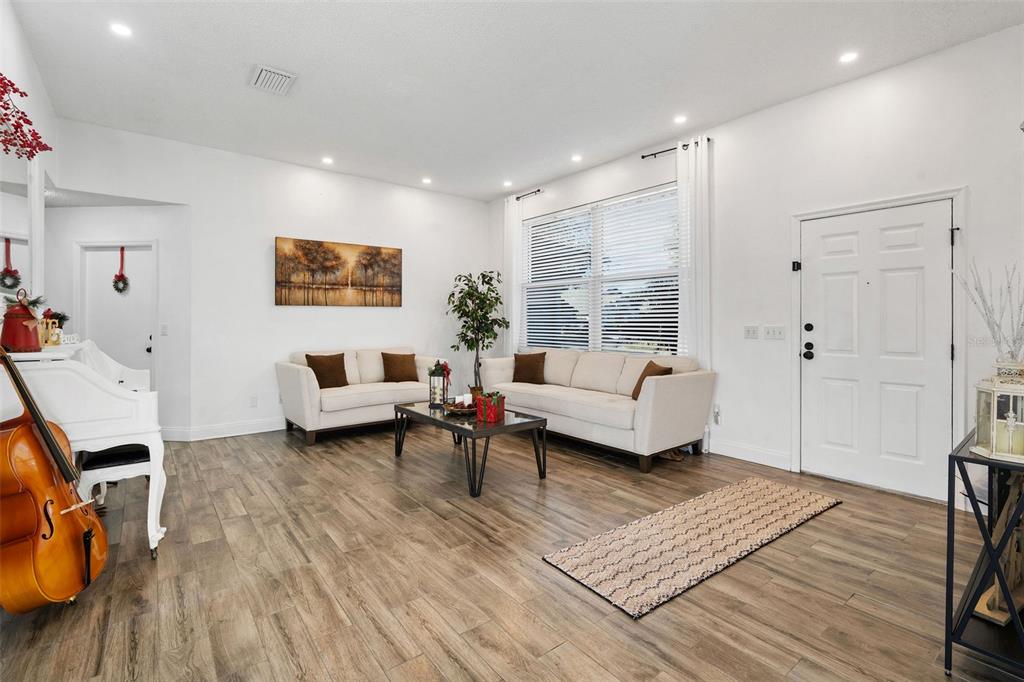 A living room features white walls, wood-look flooring, two cream sofas, and a cello — 15101 REDVALE DRIVE, TAMPA, FL