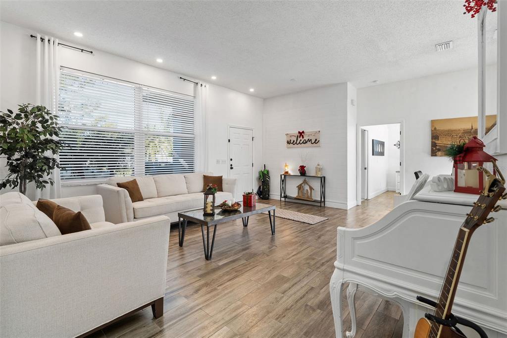A bright living room features white walls, wood-look flooring, a white sofa, and large windows — 15101 REDVALE DRIVE, TAMPA, FL
