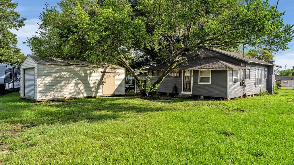 A gray house with a detached shed sits on a grassy lot under large trees — 1232 WRIGHT DRIVE, LAKELAND, FL