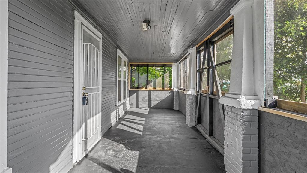 A covered porch with gray painted wood siding, a white door, and brick column supports — 1232 WRIGHT DRIVE, LAKELAND, FL