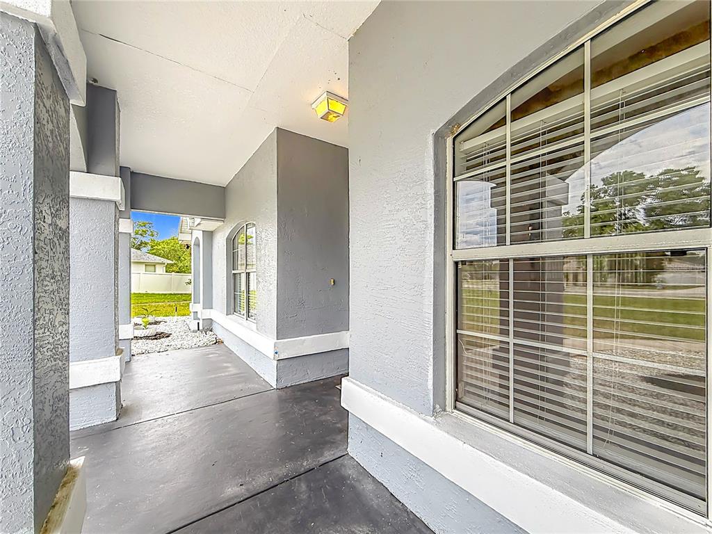 A covered gray porch features a large window with blinds and a ceiling light fixture — 4319 NW 4TH CIRCLE, OCALA, FL