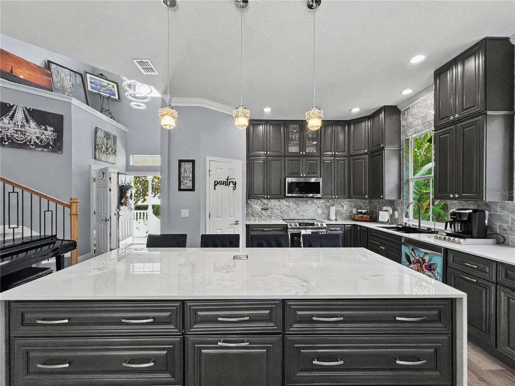 A kitchen features dark cabinetry, a large white quartz island, and three hanging pendant lights — 816 RUNNER OAK STREET, CELEBRATION, FL