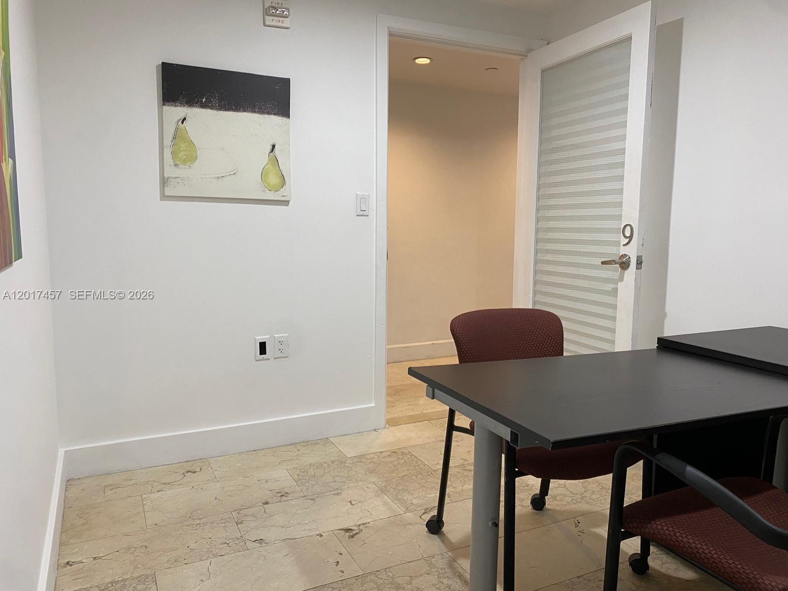 An office space features a black desk, two chairs, tile flooring, and a framed pear painting — SWEETWATER, FL