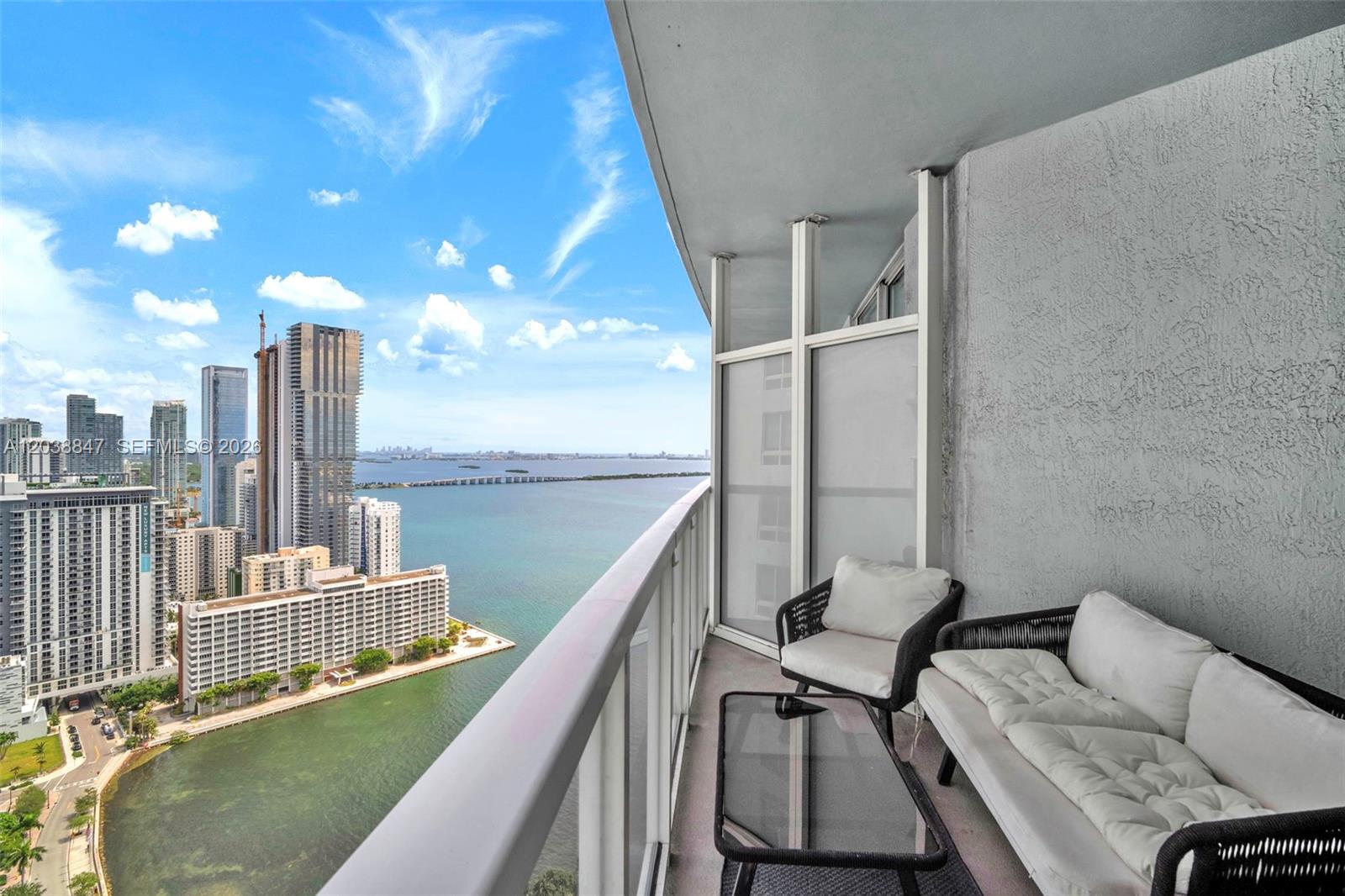 A high-rise balcony features outdoor furniture overlooking a bay and city skyline — 1900 N Bayshore Dr # 3610, Miami FL 33132, MIAMI, FL