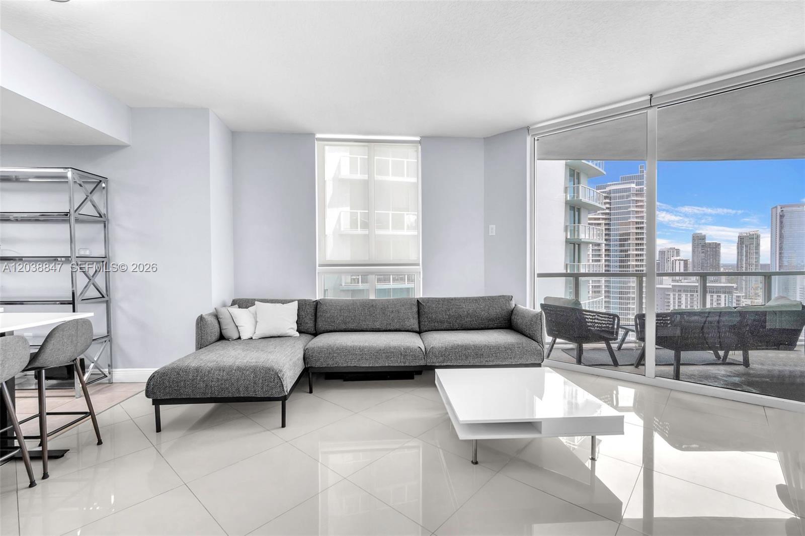 A modern living room features a gray sectional sofa, white coffee table, and balcony view — 1900 N Bayshore Dr # 3610, Miami FL 33132, MIAMI, FL