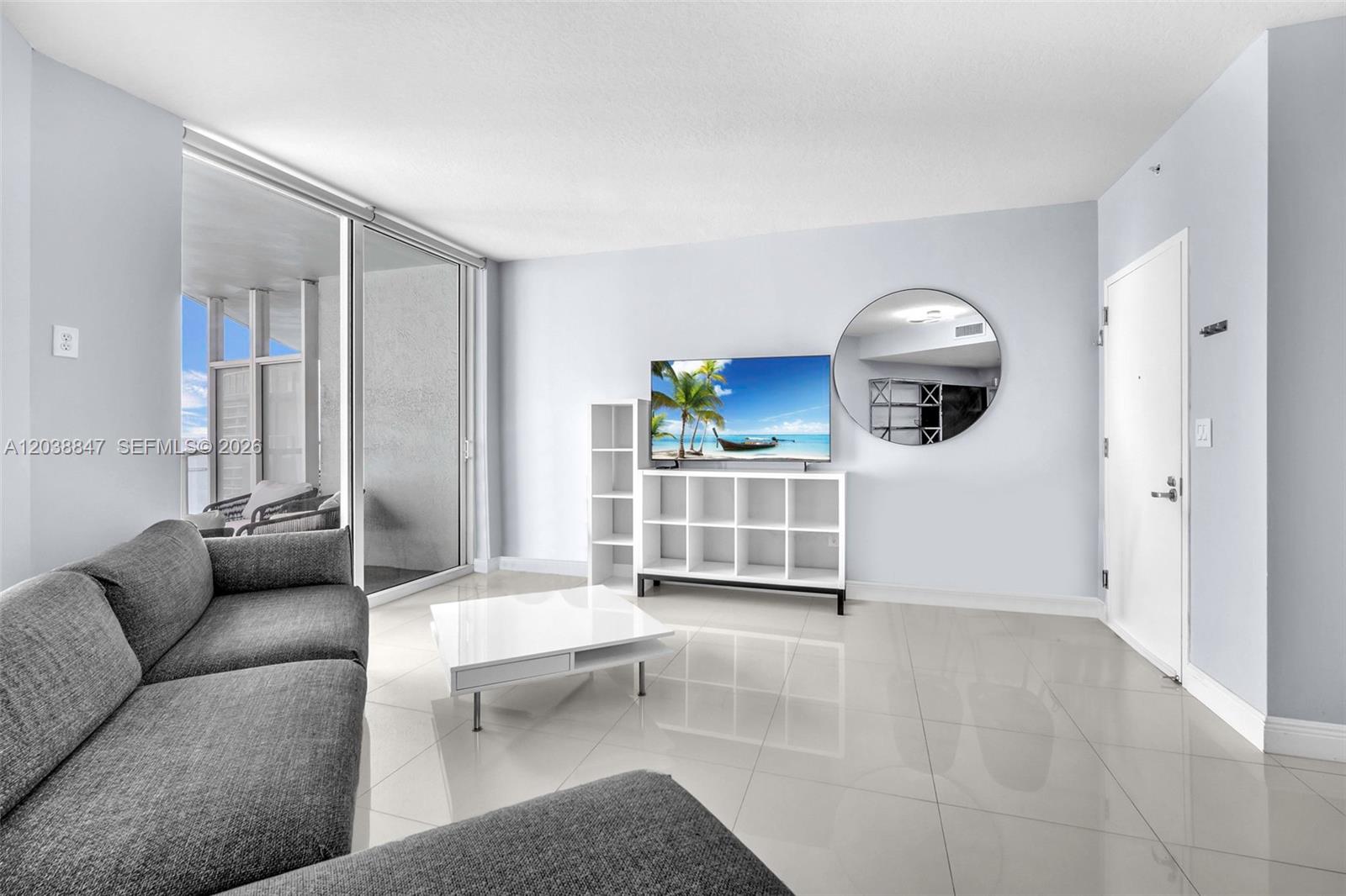 A bright living room features white tile floors, a gray sofa, and a white media console — 1900 N Bayshore Dr # 3610, Miami FL 33132, MIAMI, FL