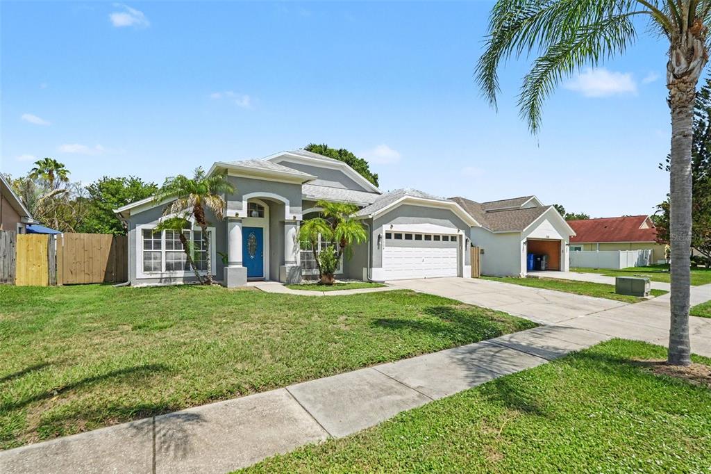 A single-story gray house with a blue front door, two-car garage, and a palm tree — 11504 WELLMAN DRIVE, RIVERVIEW, FL
